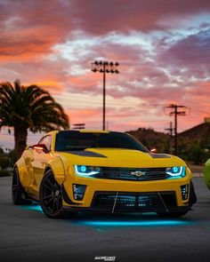 a yellow sports car parked in a parking lot at dusk with the sun setting behind it