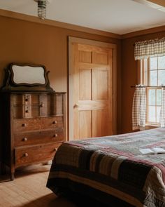 a bed sitting in a bedroom next to a wooden dresser and window covered with curtains