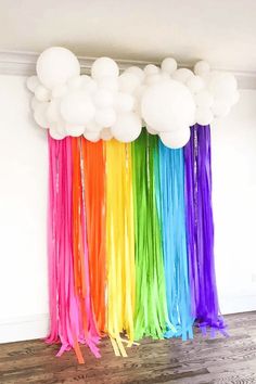 balloons and streamers are hanging from the ceiling in front of a rainbow colored wall