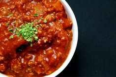 a white bowl filled with meat covered in sauce and garnished with parsley