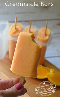 an orange popsicle is being held up by someone's hand with the popsicle in front of them