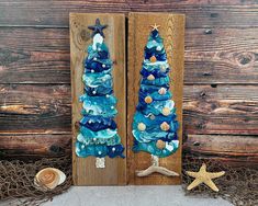 two blue christmas trees on wooden boards with shells and seashells next to them