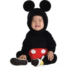 a baby in mickey mouse costume sitting on the ground with his feet up and smiling