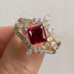 a woman's hand holding a ring with a red stone surrounded by white diamonds