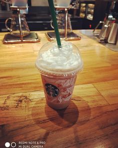 a starbucks drink with whipped cream and a green straw sitting on top of a wooden table