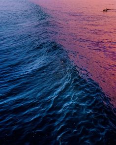 the water is pink and blue as it begins to rise up into the sky at sunset