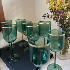 green wine glasses sitting on top of a table next to a vase with flowers in it