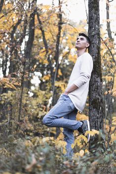 a young man standing on his knees in the woods, leaning against a tree trunk