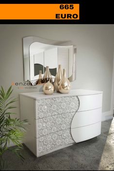 a white dresser with two gold vases on top and a mirror above it in the corner