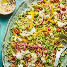 a salad on a platter with a fork and bowl of dressing in the background