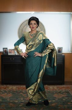 a woman in a green and gold sari posing for the camera with her hands on her hips