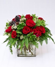 a glass vase filled with red roses and greenery on top of a white table