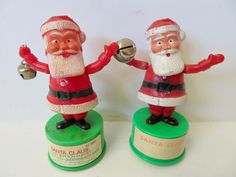 two santa claus figurines on top of green bases with bells in their hands