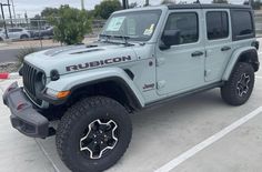 a light blue jeep parked in a parking lot next to a building with a sign that says rubicon on it