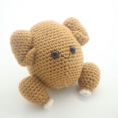 a crocheted teddy bear with big eyes sitting on a white surface, looking at the camera