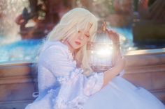 a woman in white dress holding a bird cage with light shining on her face and chest