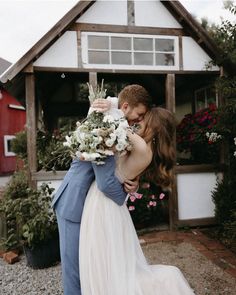 a bride and groom hugging in front of a red barn with flowers on the ground