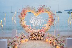 a heart - shaped sign that says will you marry me? surrounded by flowers and candles