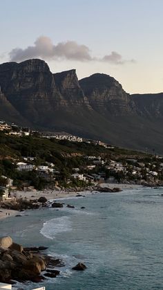 a beach with mountains in the background and houses on the shore near water's edge