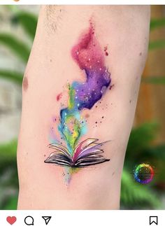 an open book tattoo on the side of a woman's leg with watercolor paint splatters