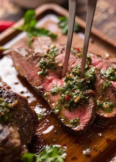 a steak is being cut with a knife on a cutting board and garnished with herbs