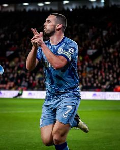 a man in blue uniform standing on top of a soccer field with his hands together