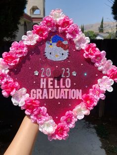 someone holding up a pink hello kitty graduation cap with flowers around it that says hello graduation