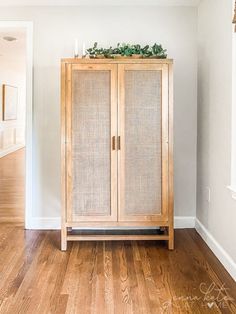 a wooden cabinet sitting in the corner of a room with white walls and wood floors