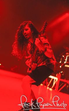 a woman with long hair playing an electric guitar in front of red lights on stage