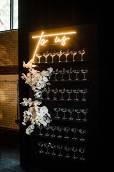 a lighted sign that says for us with wine glasses and flowers