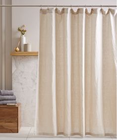 a white shower curtain in a bathroom next to a wooden shelf with towels on it