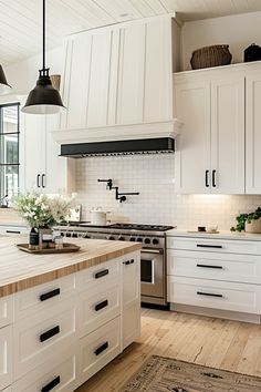 a large kitchen with white cabinets and wooden flooring, along with black pendant lights