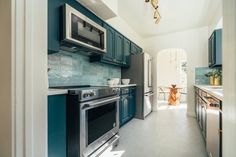 a kitchen with blue cabinets and stainless steel appliances in it's center hallway leading to the dining room