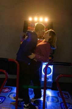 a man and woman are kissing in front of a stage with spotlights on the wall