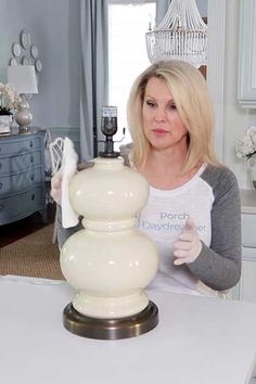 a woman standing in front of a white table with a lamp on top of it