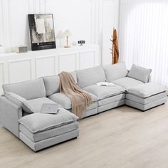 a living room with white walls and wood flooring, a large sectional couch in the middle