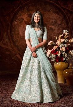 a woman in a blue and white lehenga standing next to a vase with flowers