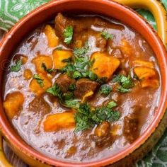 a bowl filled with stew on top of a green table cloth next to a wooden spoon