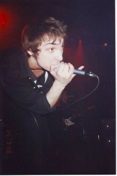 a young man singing into a microphone in front of a stage with red lights behind him