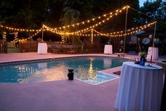 an outdoor pool is lit up with lights and table cloths for the guests to sit at