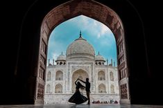 a man and woman standing in front of an arch with the tajwa mosque in the background