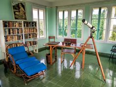 a room with green tile floors and lots of bookshelves, chairs, and a telescope