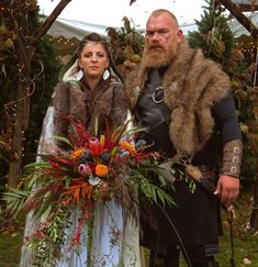 a man and woman dressed up in medieval costumes standing next to each other with flowers