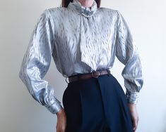 Vintage 1980s silver gray blouse , Shoulder pad blouse , Button back blouse  Please check measurements.  Bust - 40 " / 101.5 cm  Total Length 23 " / 58.5 cm  Shoulder to Shoulder 14.5 " / 36.75 cm  Sleeve 22 " / 56 cm  Condition: Excellent Vintage Condition  No noticeable stains, tears or holes.  Detail  - High neck collared  - long sleeve  - Shoulder pad blouse  - Button back blouse  - No lining  Materials  - 100 % Polyester    Our clothes are vintage products. well cleaned  please believe  And I have checked the quality before selling. We do our best to check for flaws or defects. But if the bug escapes our investigation. accidentally  I'm so sorry  and please let us know ASAP  We will do our best to resolve the situation.  If you have any questions about product details  or need more pr Cocktail Blouse, Blouse High Neck, Silver Blouse, Gray Blouse, Metallic Blouses, High Neck Blouse, Feminine Blouses, Grey Blouse, Blouse Long Sleeve