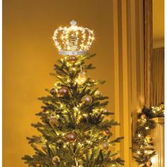 a small christmas tree with lights on it and a crown hanging from the top, in front of a window