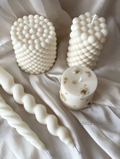 two white vases sitting next to each other on top of a bed covered in white sheets