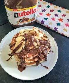 a stack of pancakes covered in chocolate syrup and peanut butter on a plate next to a jar of nutella