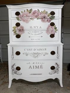 a white dresser with pink flowers painted on the top and bottom drawers, in front of a garage door