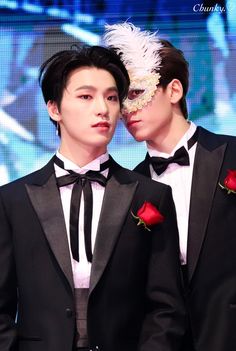 two young men in tuxedos with one wearing a mask and the other holding a rose