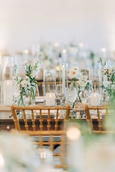 the table is set with clear vases, candles and white flowers on top of them